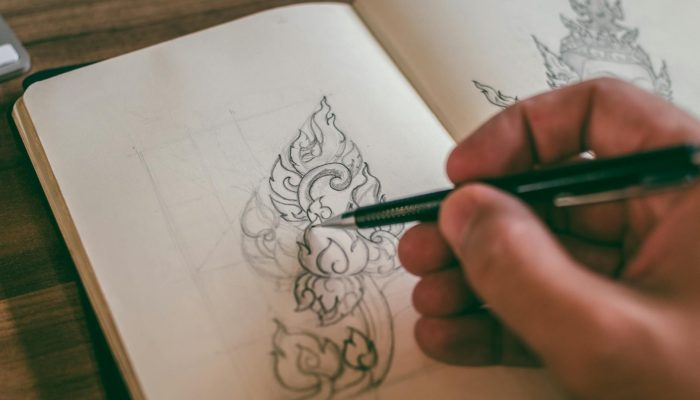 Close-up of a hand sketching detailed design in a sketchbook with mechanical pencil.